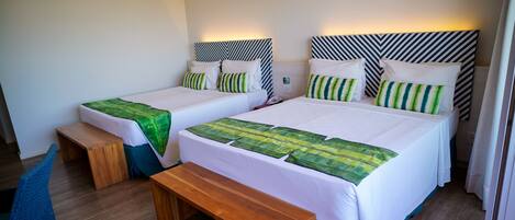 A hotel room with two beds, each with a green leaf-patterned bedspread, a wooden bench, and a patterned headboard.