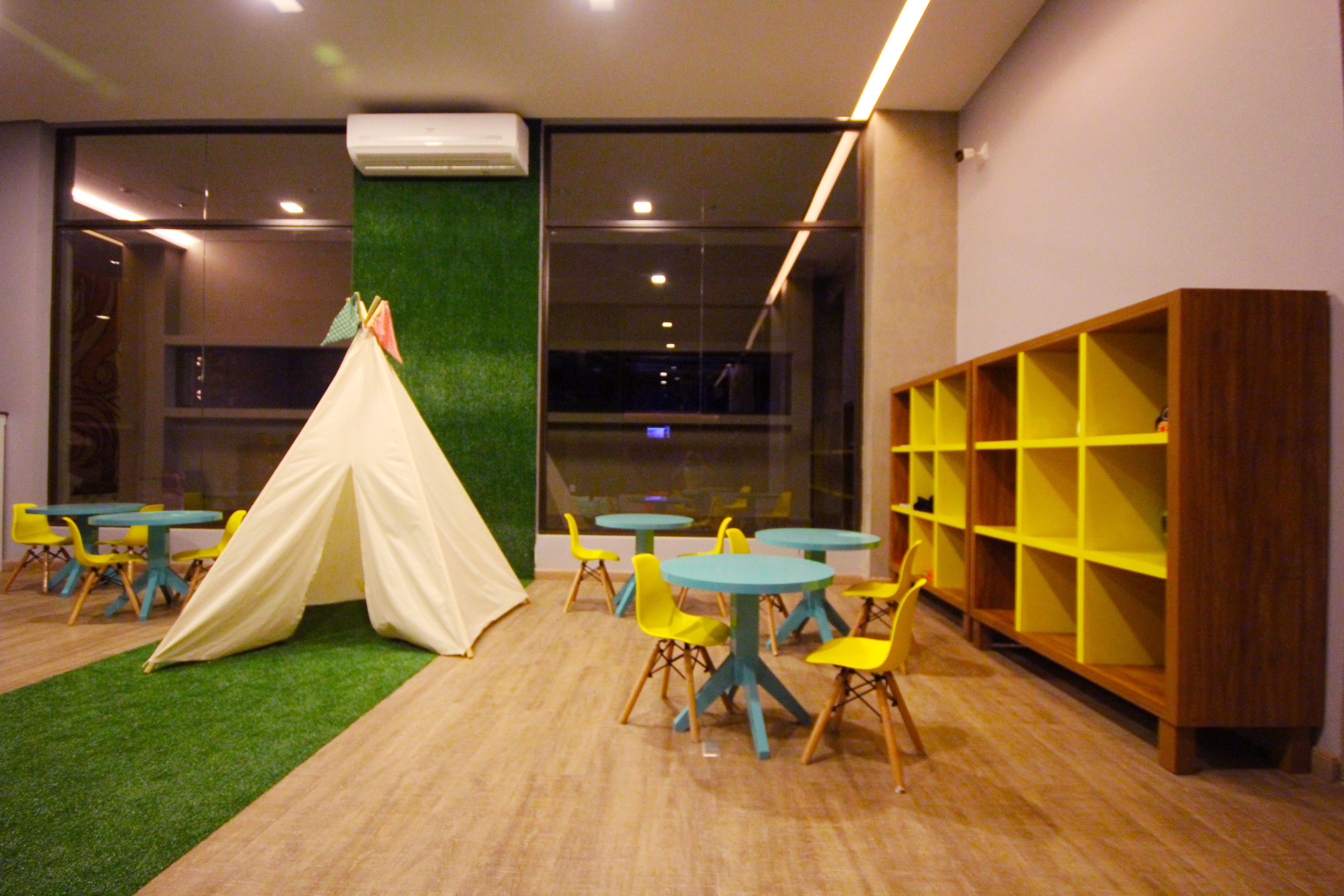A room with a tent, tables, chairs, and a bookshelf.
