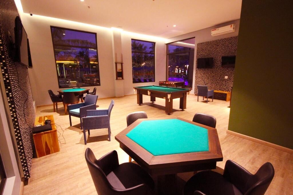 A pool table with surrounding chairs, a billiards table, and large windows offering a view of the outdoors.
