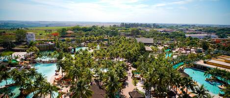 A resort with multiple swimming pools, palm trees, and a view of the surrounding countryside.