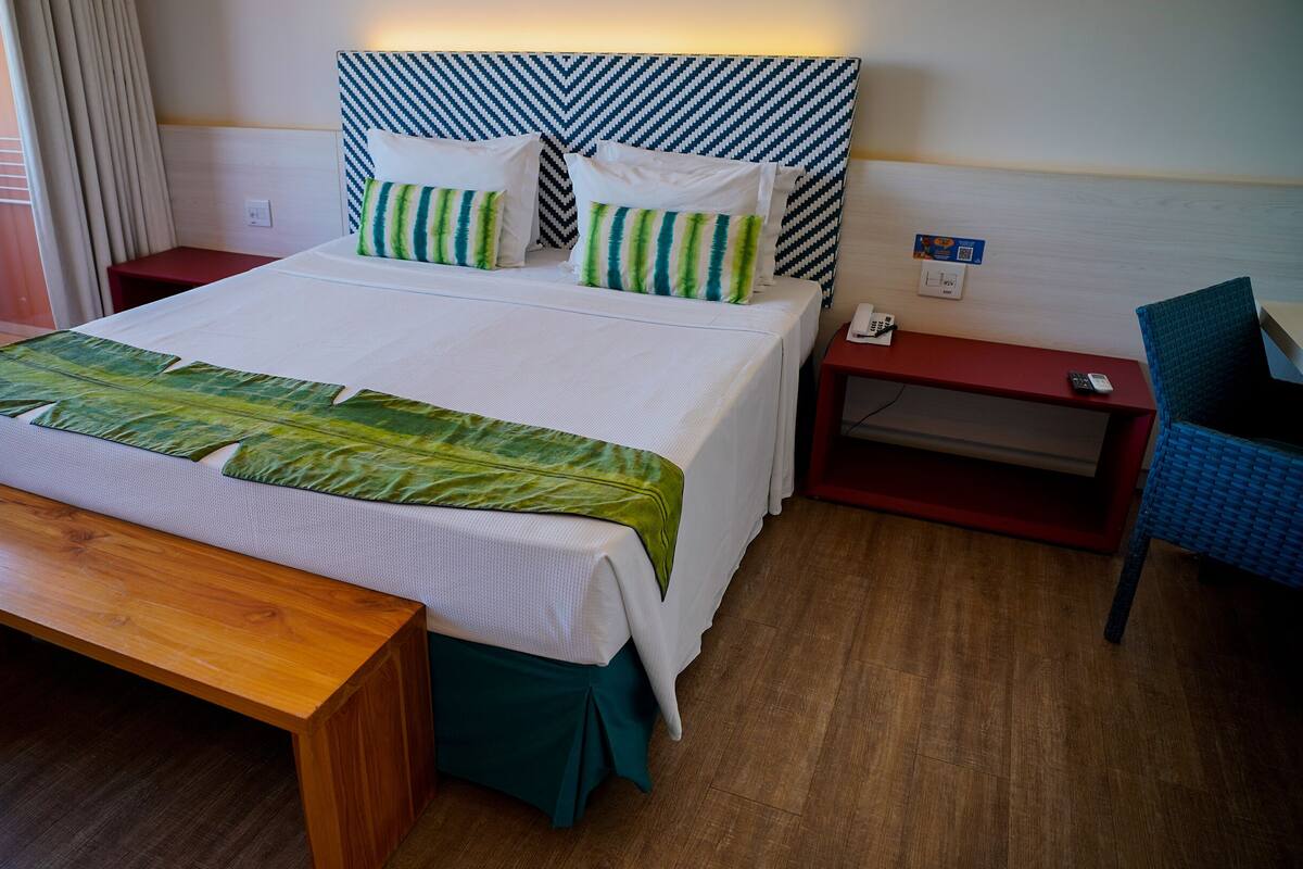 Une chambre d’hôtel avec un lit, une table de chevet avec un téléphone, une chaise et un banc.