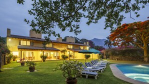 Ein helles Haus mit Swimmingpool, Liegestühlen und Topfpflanzen.