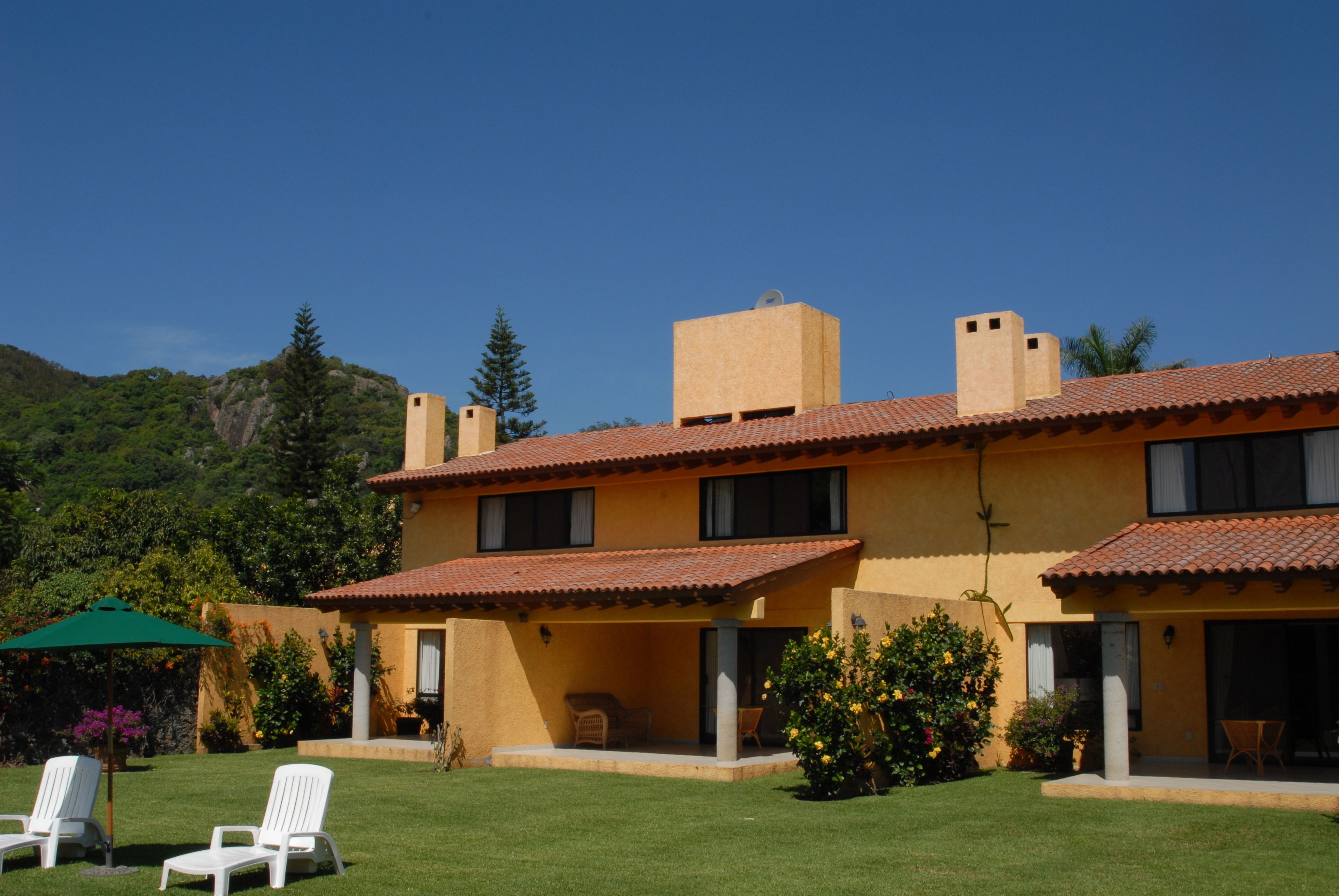 A two-story house with a tiled roof, a covered patio with outdoor furniture, and a well-maintained lawn.