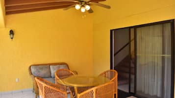Una habitación con una mesa de vidrio, sillas de mimbre, un ventilador de techo, un sofá y una puerta corredera de cristal.