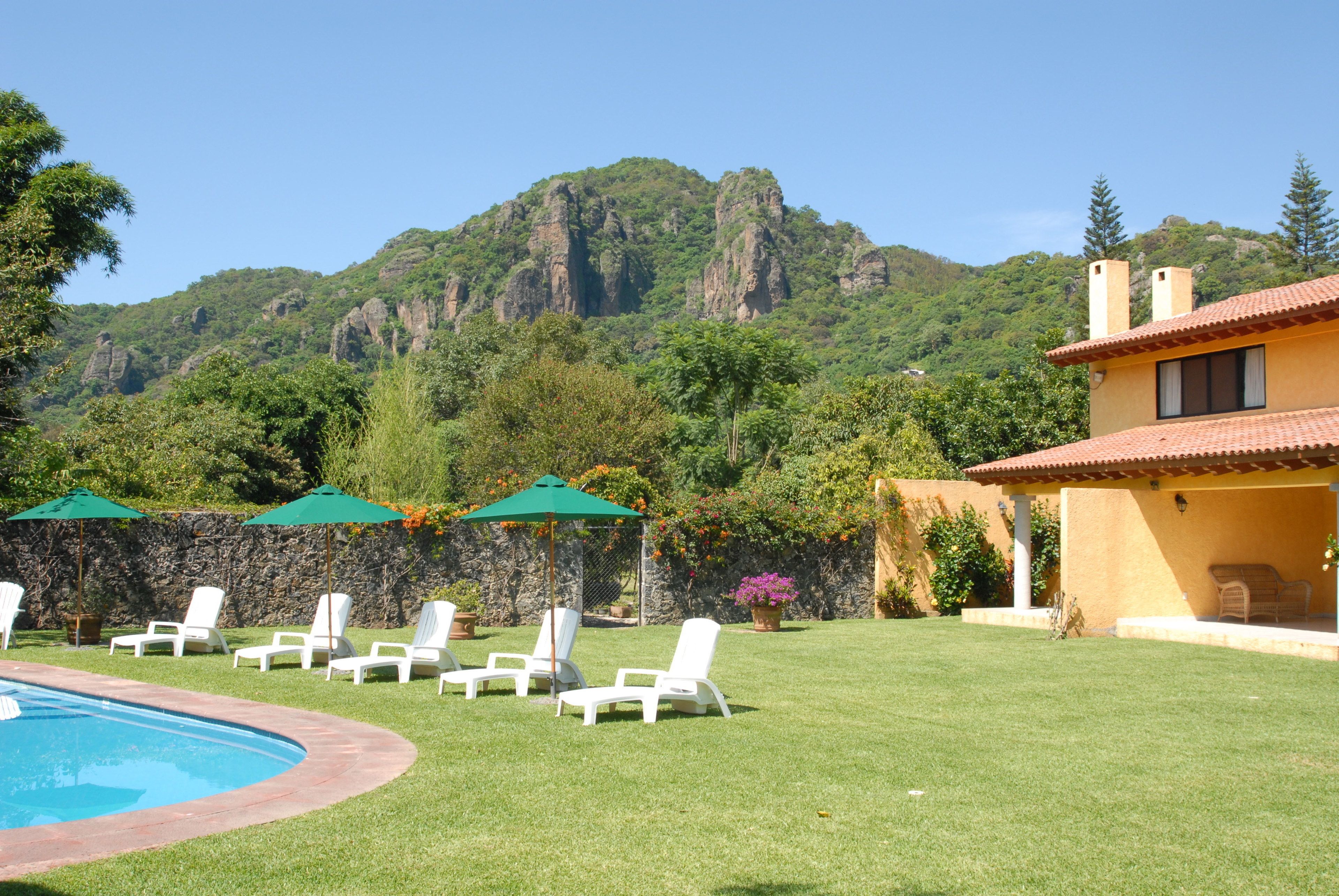 A pool area with lounge chairs and umbrellas, a stone wall, and a mountain backdrop.