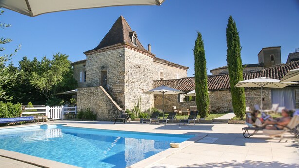 A stone building with a swimming pool, outdoor seating, and a clear blue sky. - Chambres d'hôtes - Les Vents Bleus (Donnazac)