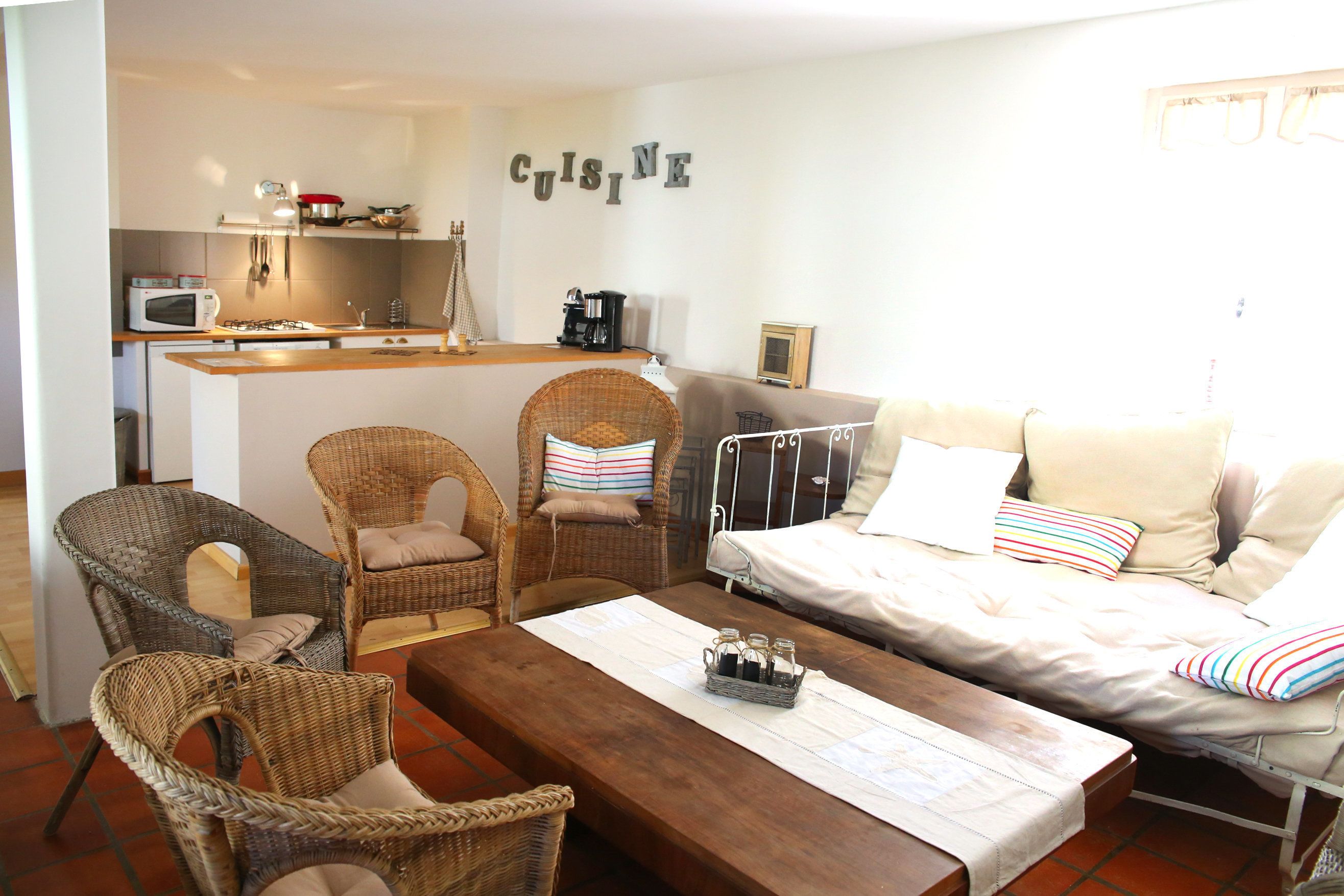 Una sala acogedora con muebles de mimbre, una mesa de centro de madera y una kitchenette al fondo.