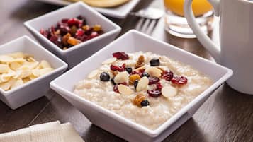 Un desayuno con avena cubierta de almendras y bayas, un cuenco de frutas secas y un vaso de zumo de naranja.