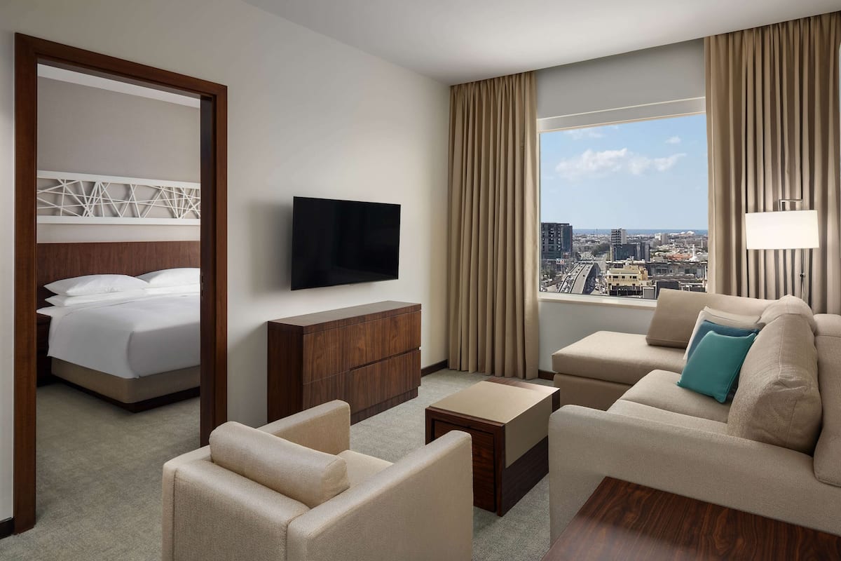 Habitación de hotel con cama, televisor, sofá y vistas a la ciudad.