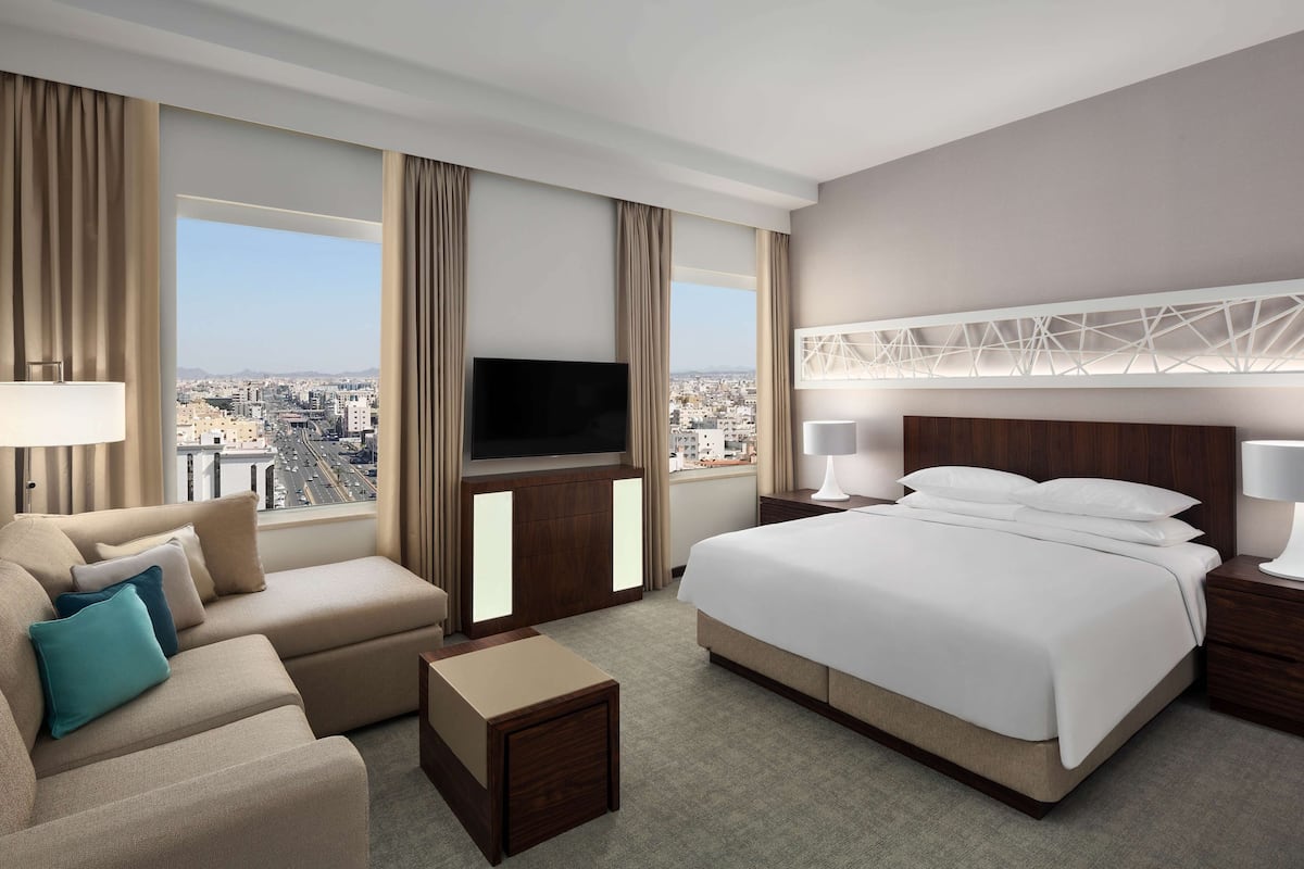 Una habitación de hotel moderna con una cama grande, un sofá, un televisor y vistas a la ciudad.