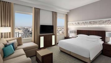 A modern hotel room with a large bed, a sofa, a TV, and a city view.