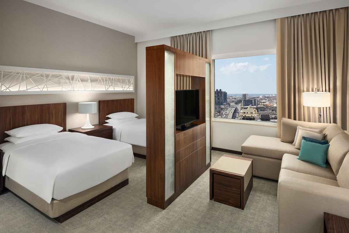 Habitación de hotel con dos camas, televisión, sofá y vista a la ciudad.