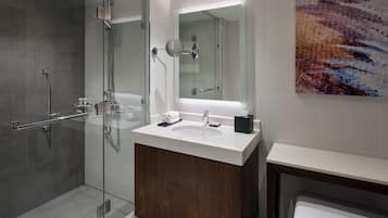A modern bathroom with a glass shower enclosure, a wooden vanity, a large mirror, and a contemporary artwork on the wall.