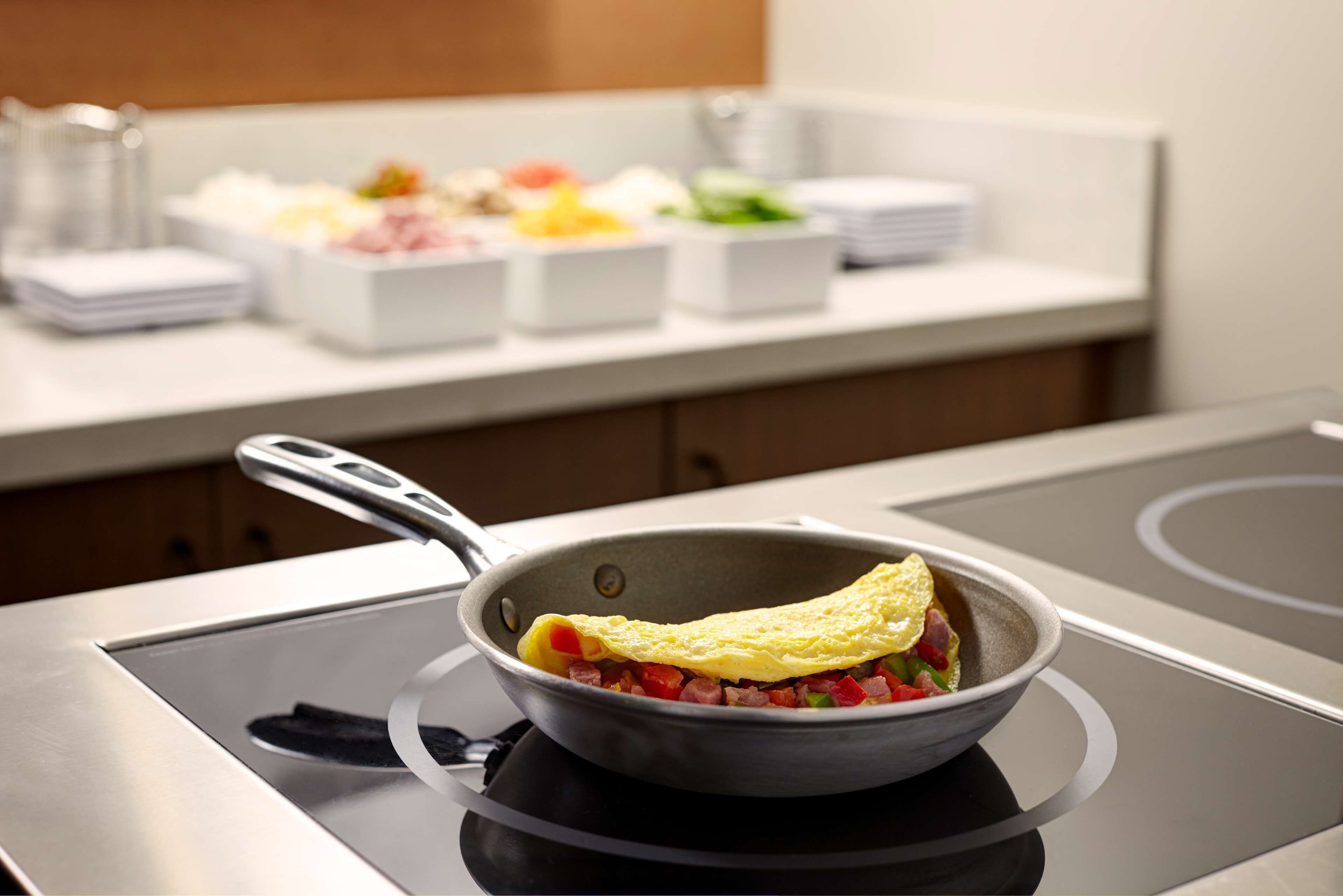 Een keuken met een pan op een inductiekookplaat, een wit aanrecht met diverse etenswaren in schalen, en een stapel witte borden.