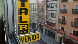 Una vista de carrer amb un senyal groc que diu "VENIDA" i un edifici amb balcons i un rètol "La Tribuna".