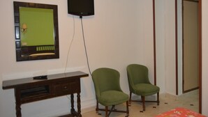 Habitació amb escriptori, dues cadires verdes, televisió de pantalla plana penjada a la paret i mirall.