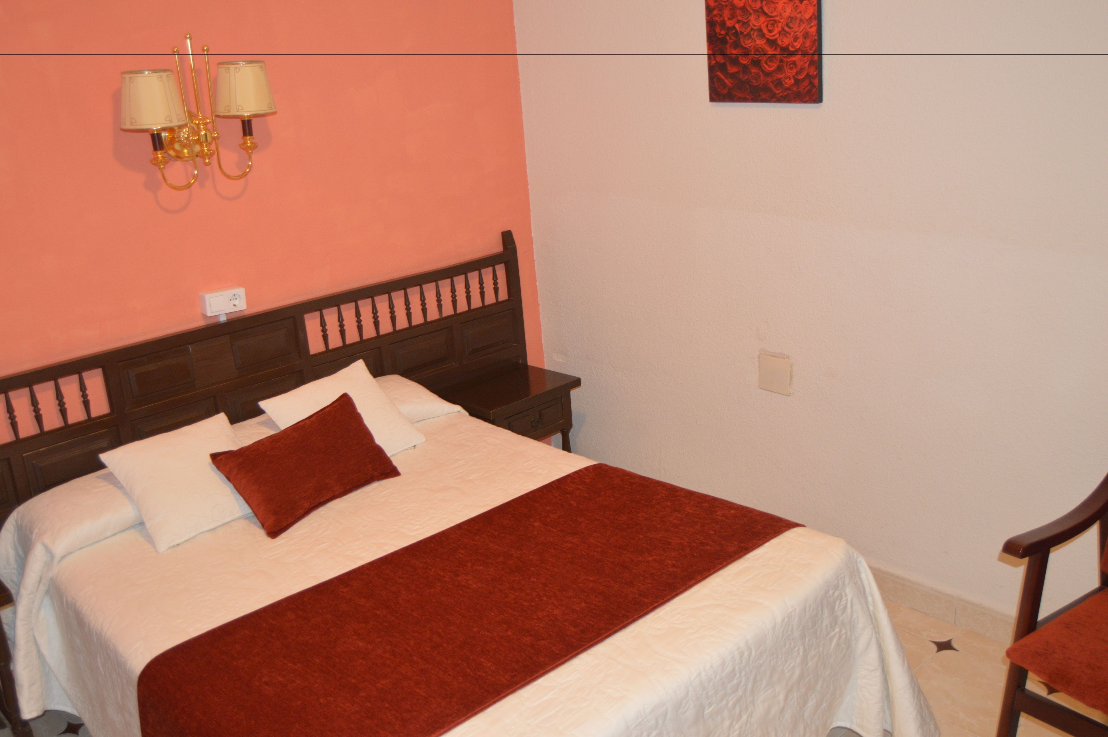 A neatly made bed with a red throw blanket, a wooden headboard, and two bedside lamps.