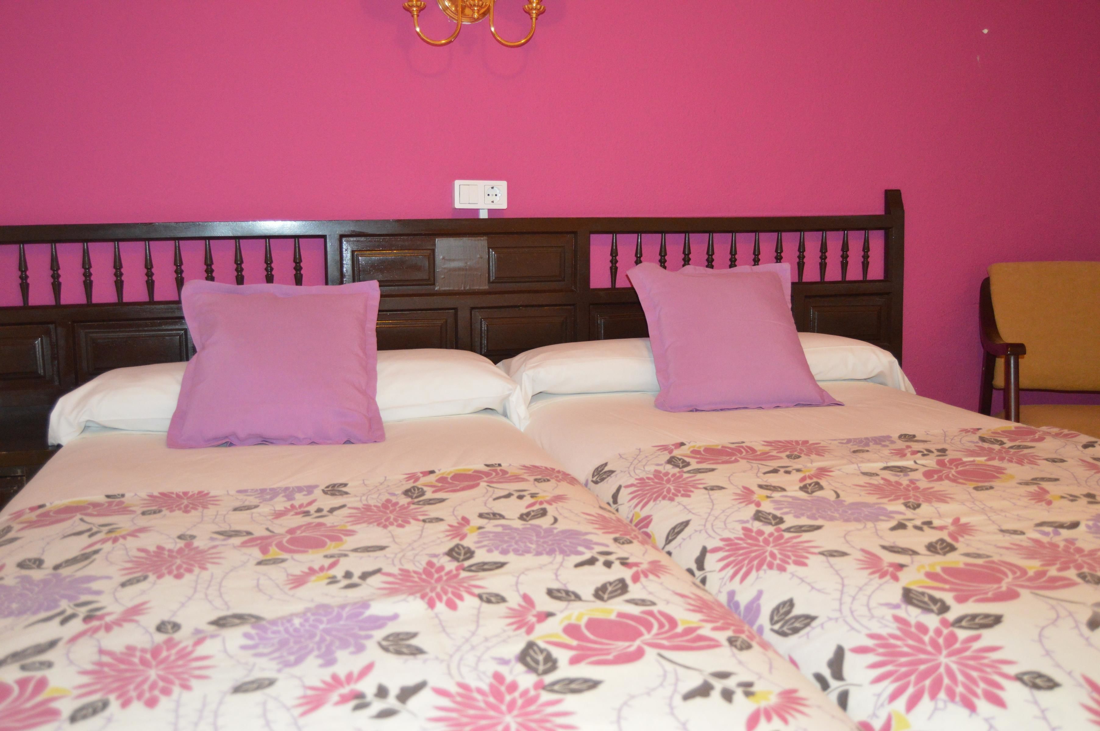 A double bed with floral bedding and two pillows, a wooden headboard, and a wall socket.
