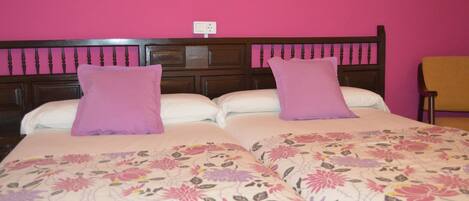 A double bed with floral bedding and two pillows, a wooden headboard, and a wall socket.