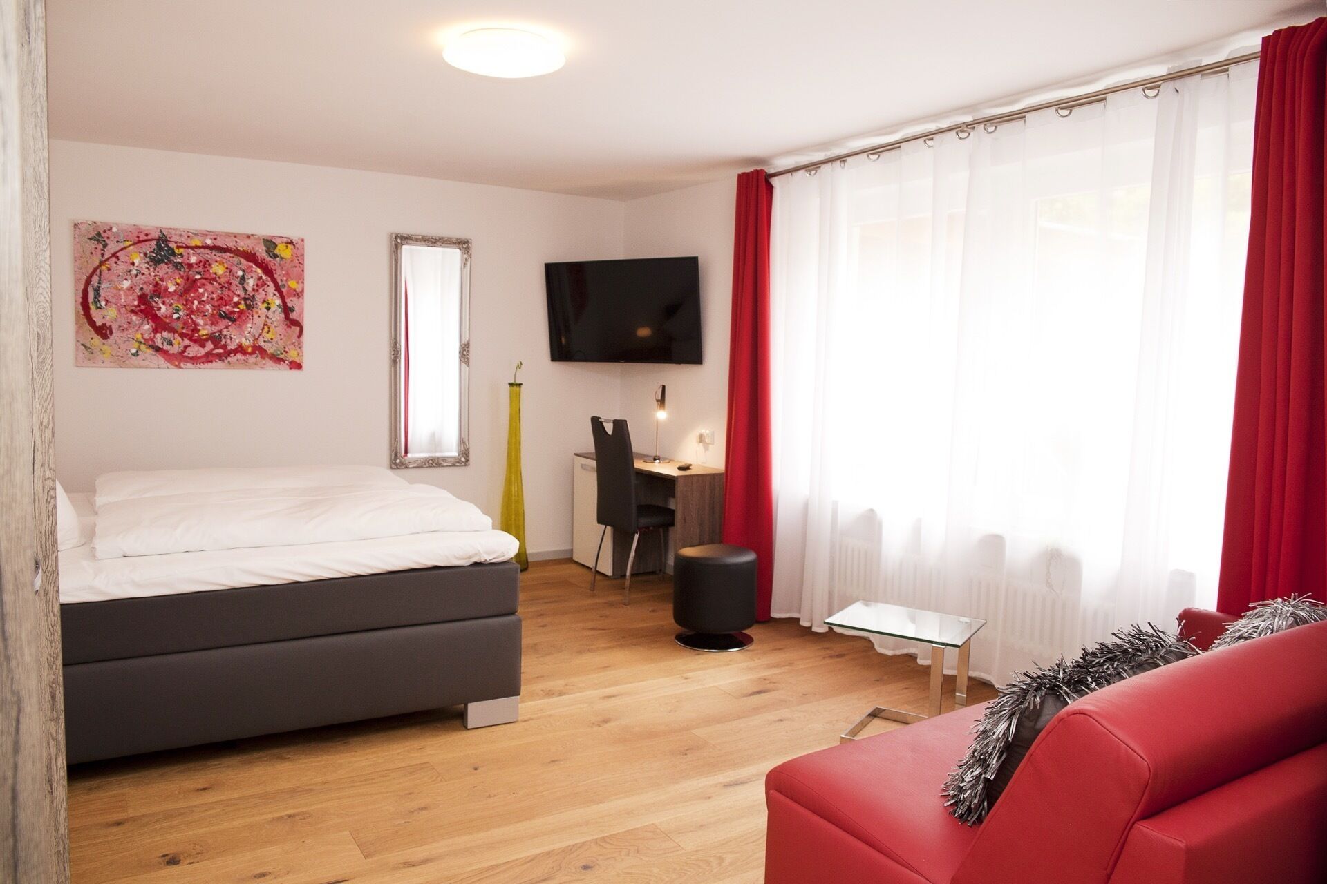 Un dormitorio moderno con una cama, un escritorio, un televisor y un sofá rojo.