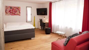 Un dormitorio moderno con una cama, un escritorio, un televisor y un sofá rojo.
