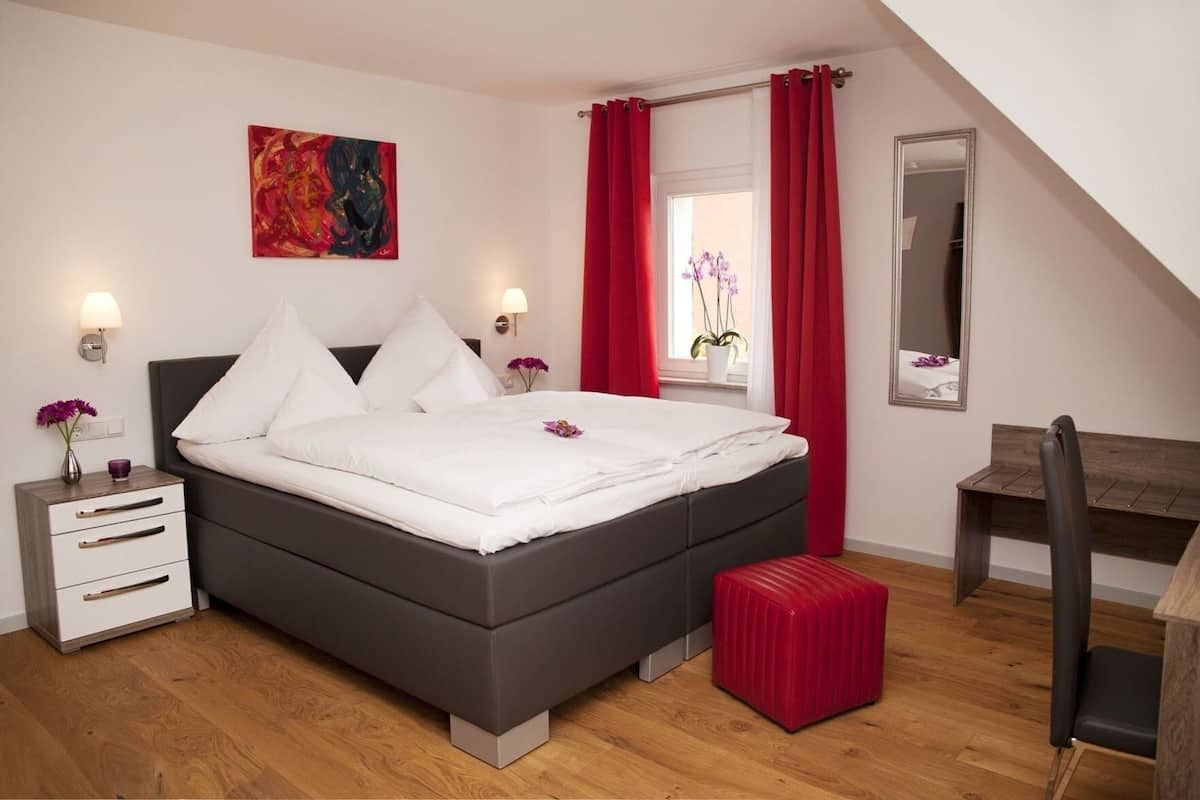 A modern bedroom with a bed, bedside tables, a desk, and a red curtain.