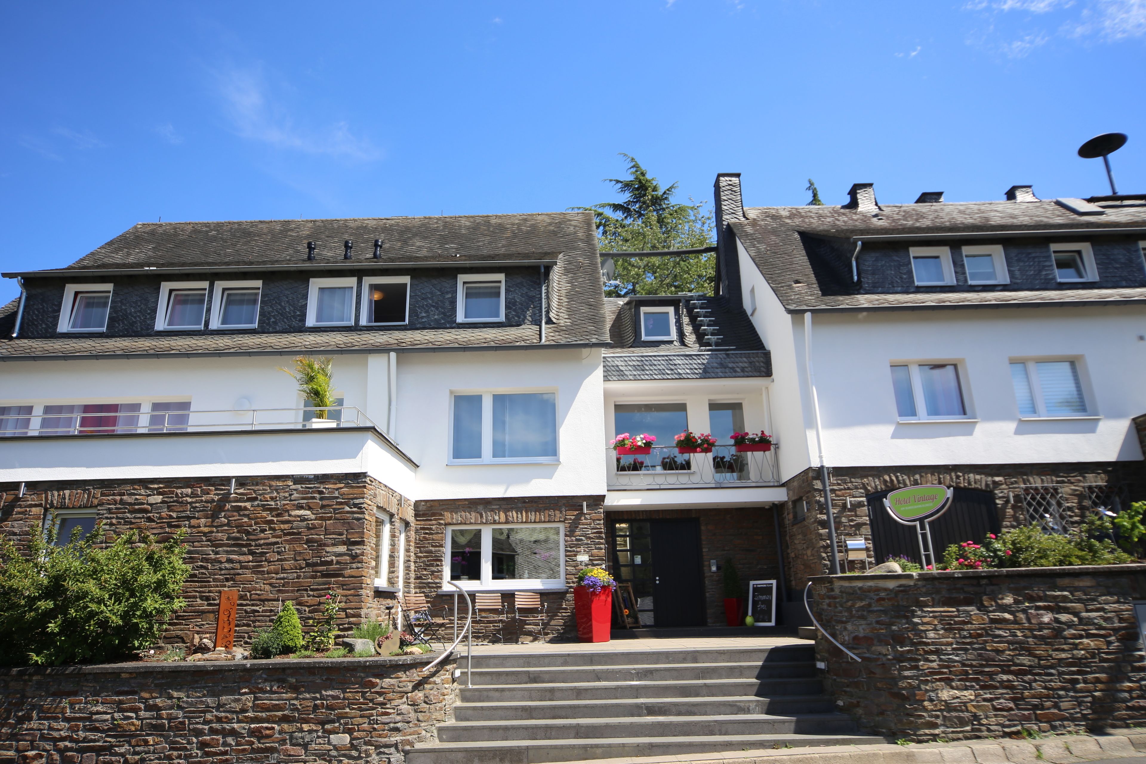 A two-story building with a stone facade, a balcony with flowers, and a sign indicating a restaurant.