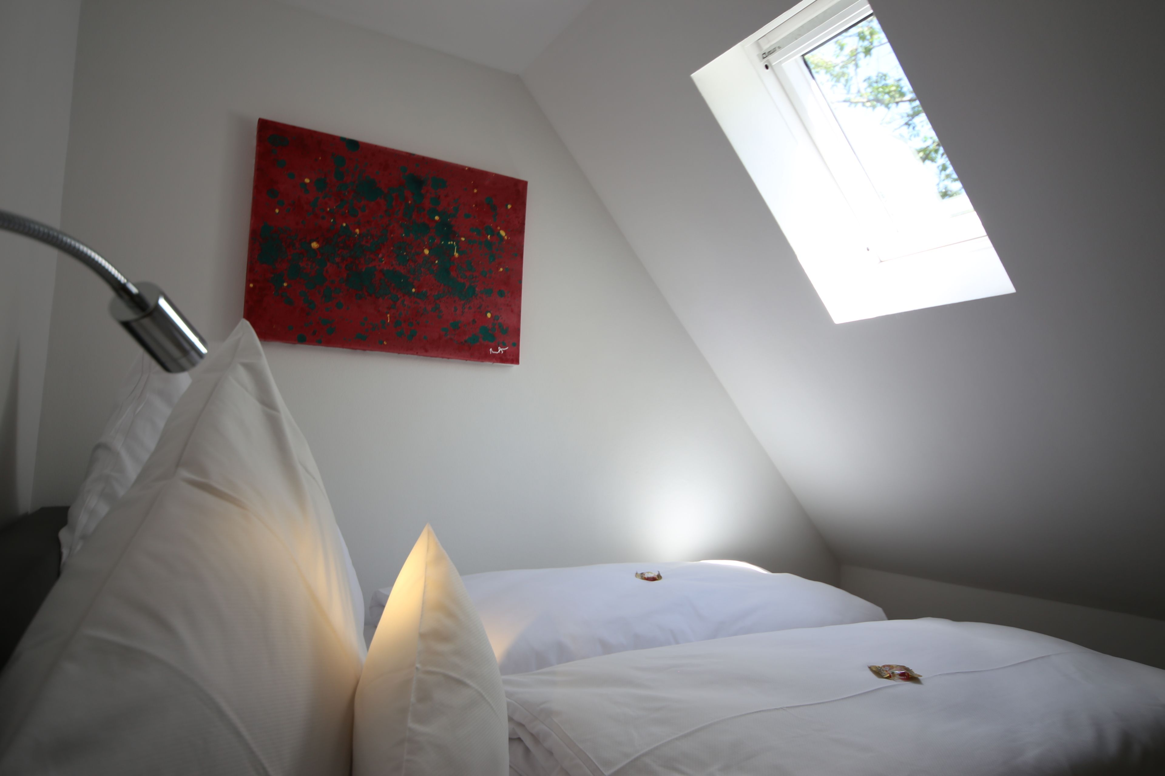 Un dormitorio con un tragaluz, un cuadro abstracto rojo y una cama con ropa de cama blanca.