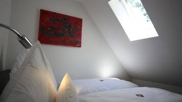 Un dormitorio con un tragaluz, un cuadro abstracto rojo y una cama con ropa de cama blanca.