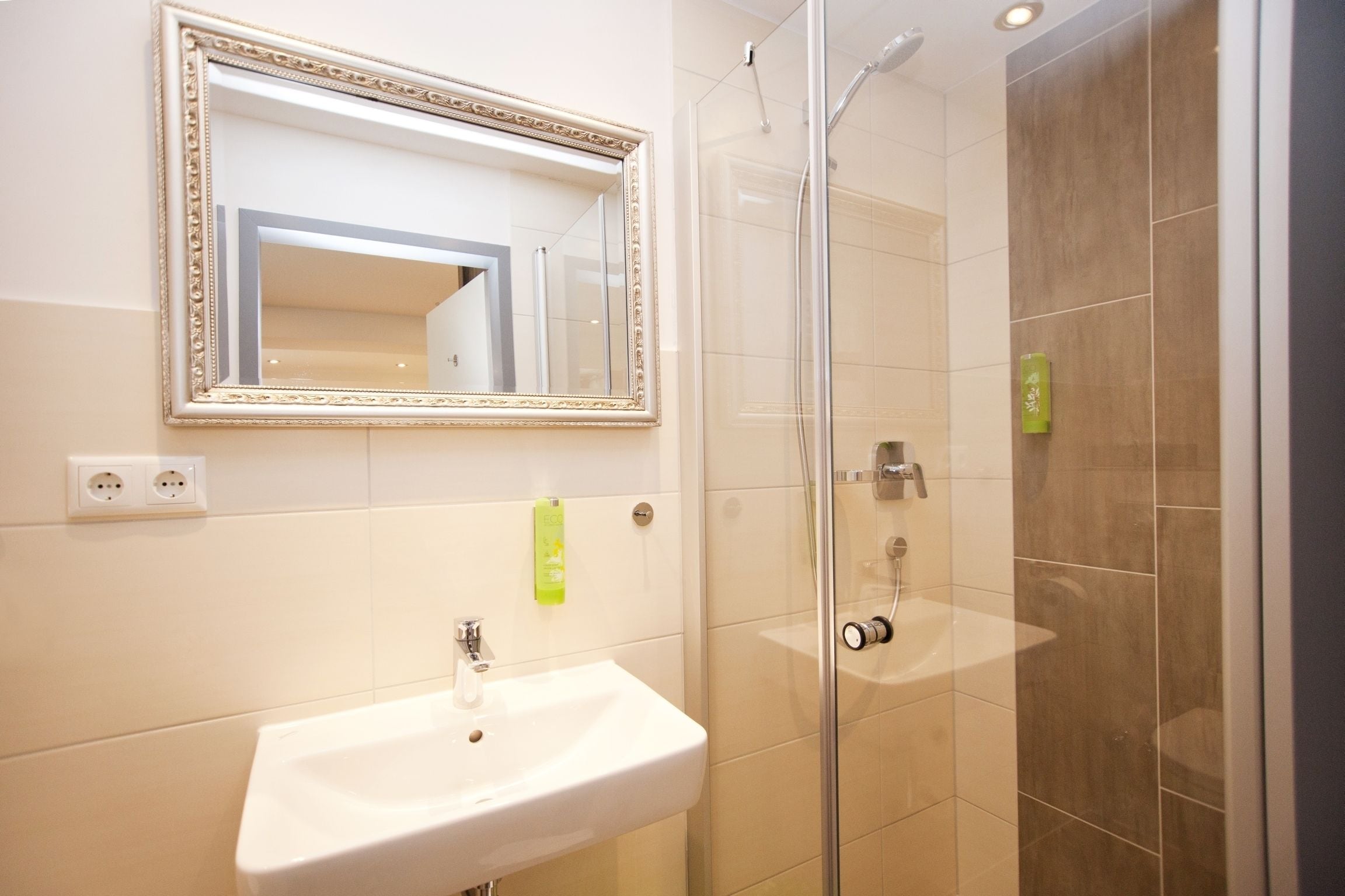 Un baño con un lavamanos blanco, un espejo con un marco decorativo y una ducha con mampara de vidrio.