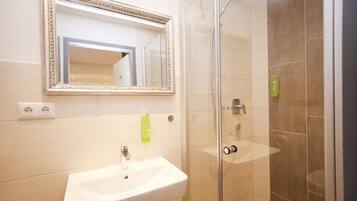 Un baño con un lavamanos blanco, un espejo con un marco decorativo y una ducha con mampara de vidrio.