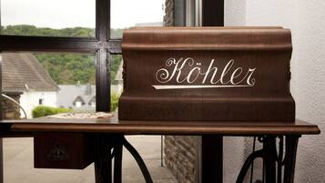 A wooden bench with the word "Köhler" engraved on it, placed in front of a window with a view of houses and greenery.