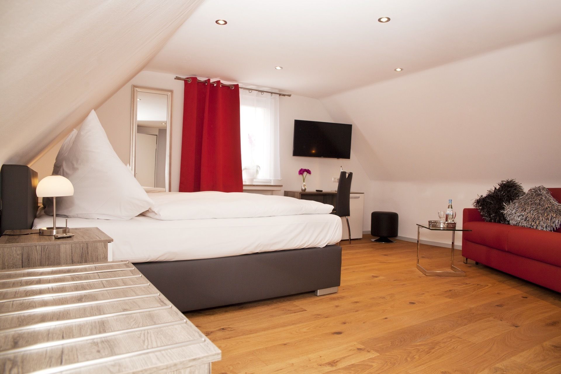 A modern bedroom with a bed, a desk, a TV, and a red sofa.