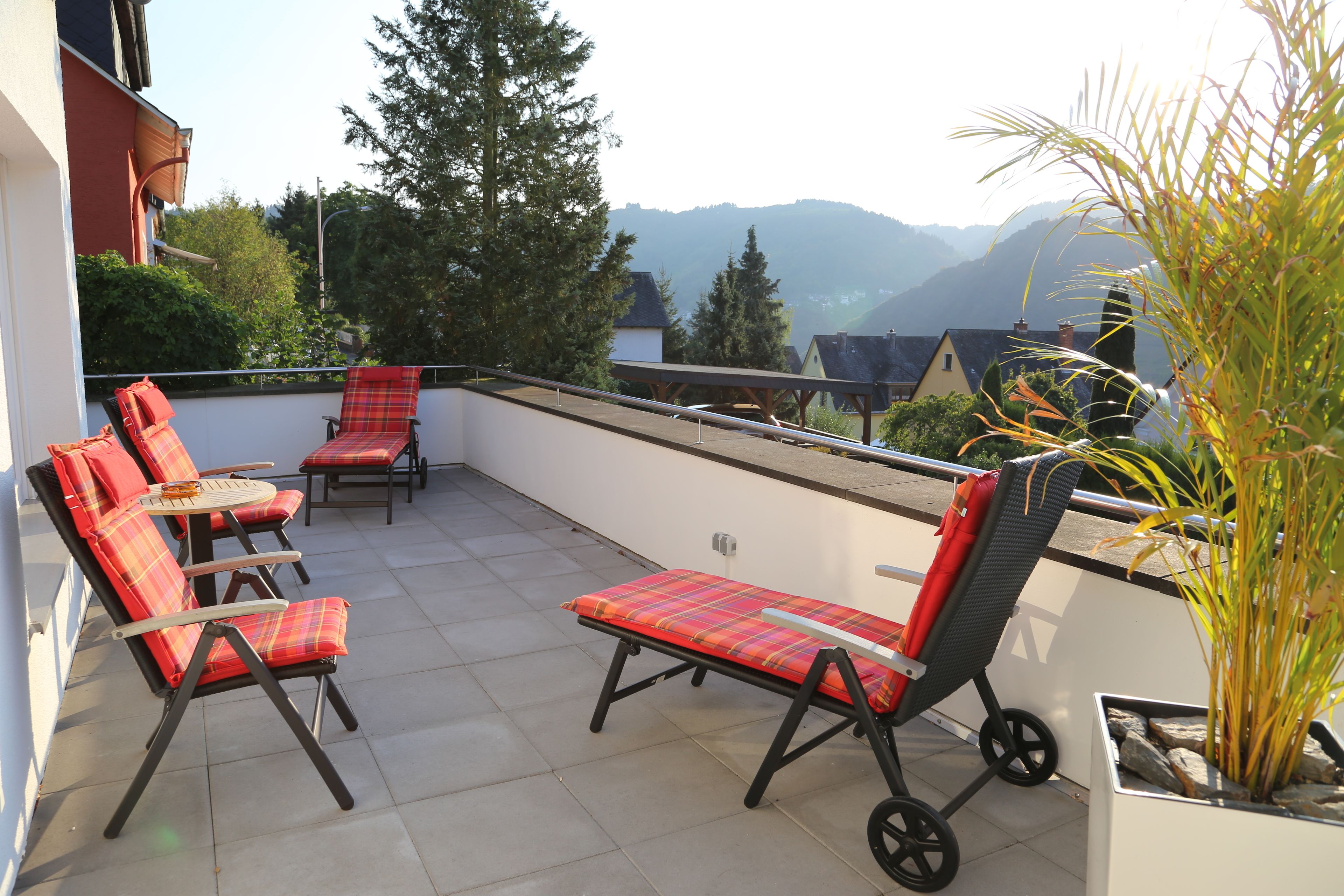 A balcony with four red and black striped chairs, a small table, and a potted plant.