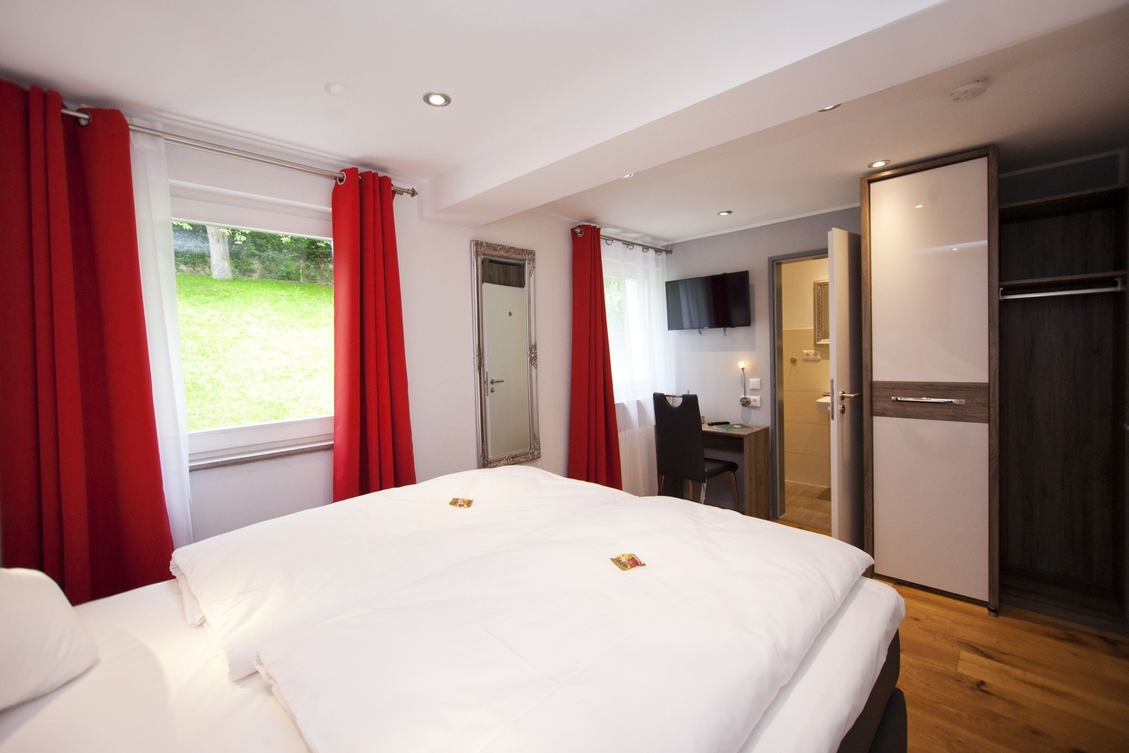 A hotel room with a large bed, a desk, a chair, and a TV.