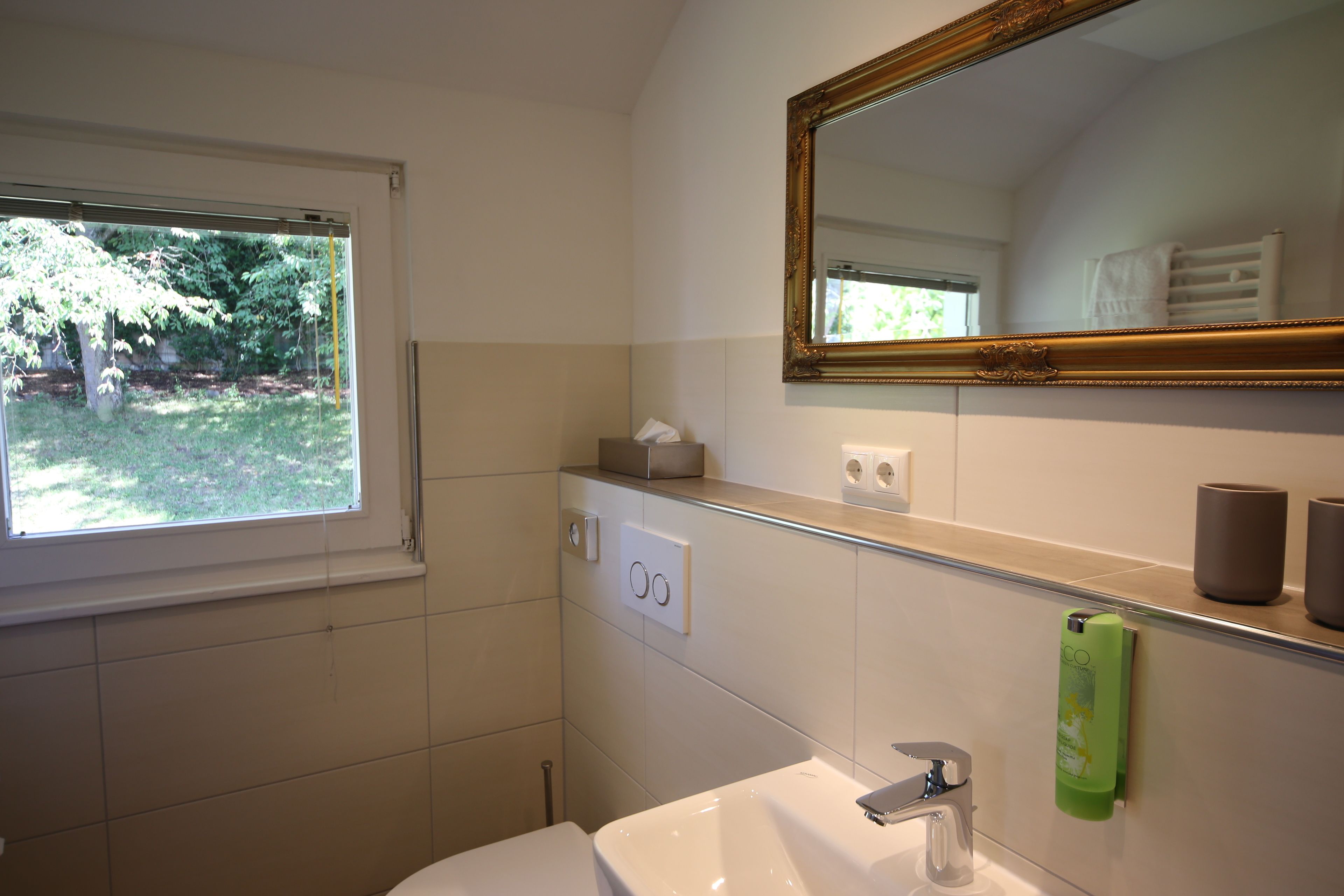 Een badkamer met raam, wastafel, spiegel en handdoekhouder.