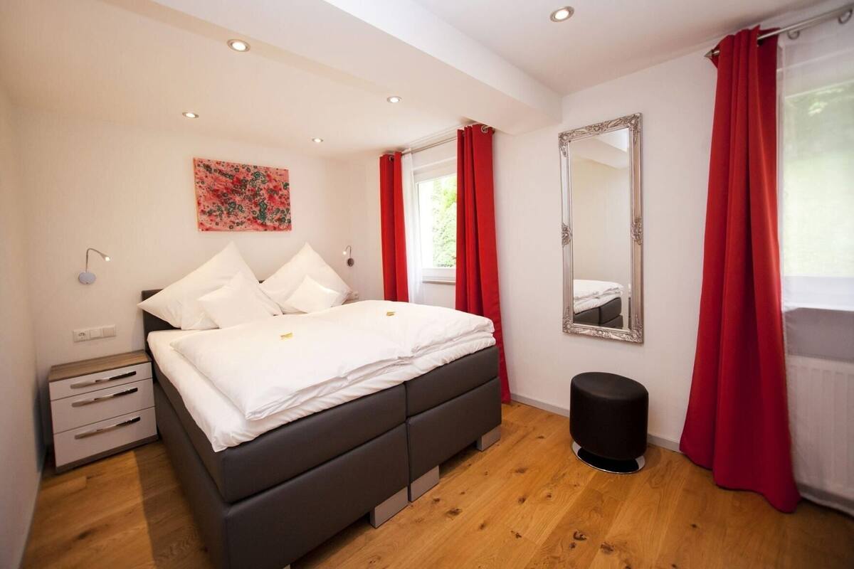 A bedroom with a bed, bedside tables, a mirror, and a red curtain.