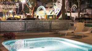 A swimming pool with lounge chairs, a water fountain, and inflatable slides in the background. - Hotel Milano (Cesenatico)