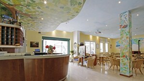 A hotel lobby with a curved reception desk, wicker furniture, and a ceiling mural. - Hotel Milano (Cesenatico)