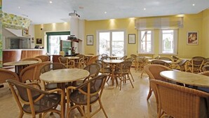 A restaurant with wicker furniture, a kitchen area, and large windows. - Hotel Milano (Cesenatico)