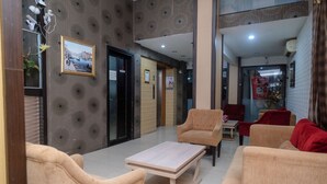 A lobby with a modern design, featuring a seating area with beige sofas and a wooden coffee table. There is a framed picture on the wall and a door with a sign. - RedDoorz Plus @ Grand Populer Hotel (Makassar)