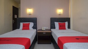A hotel room with two beds, each with a red and white bedspread, a nightstand between them, and a wall-mounted light fixture. - RedDoorz Plus @ Grand Populer Hotel (Makassar)