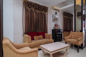 A living room with two sofas, a coffee table, and a TV stand. - RedDoorz Plus @ Grand Populer Hotel (Makassar)