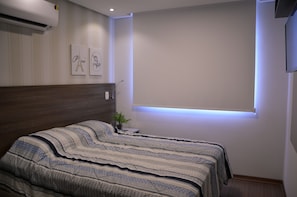 A bedroom with a bed, a nightstand, a wall-mounted air conditioner, and a window with a light fixture. - Residencial Paradiso (Gramado)
