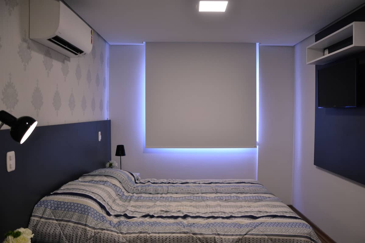 A bedroom with a bed, a wall-mounted TV, and an air conditioning unit.