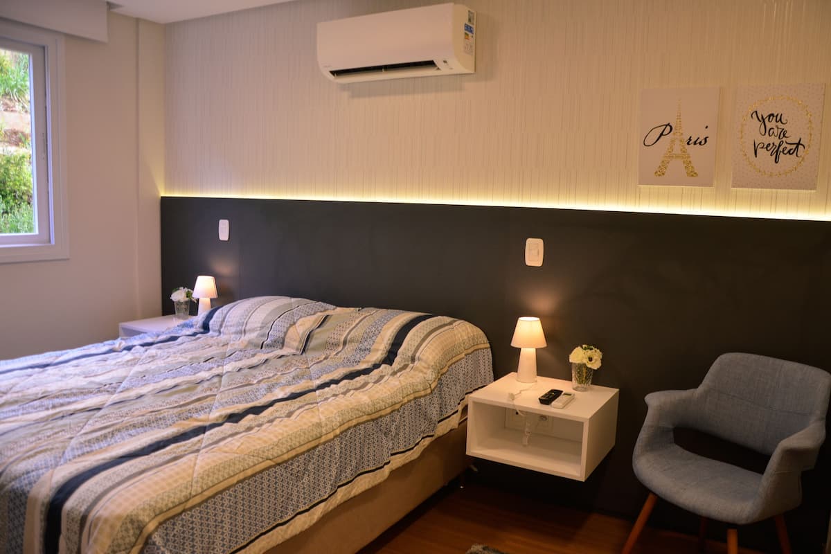 A bedroom with a bed, bedside table, lamp, chair, and wall decorations.