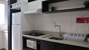 Una cocina moderna con armarios blancos, un lavamanos de acero inoxidable, una estufa a gas y un microondas.