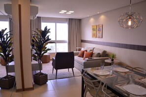 A modern living room with a dining area, large windows, and a ceiling light fixture. - Residencial Paradiso (Gramado)