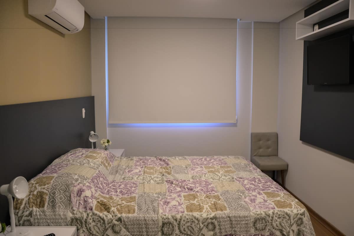 A bedroom with a bed, bedside table, lamp, and a TV mounted on the wall.