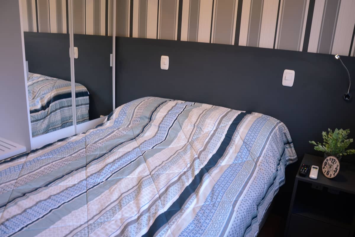 A bed with a striped bedspread, a bedside table with a clock and a plant, and a wall with a striped pattern.